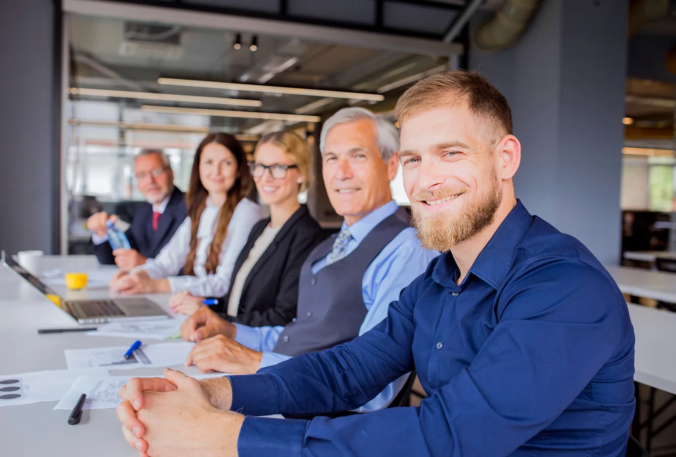 Groupe de professionnels assis autour d'une table, souriant et regardant l'objectif.