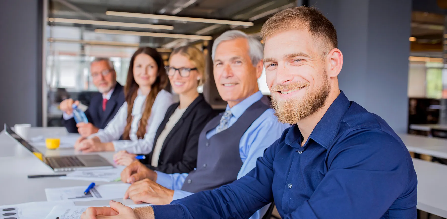 Cinq personnes souriantes en réunion autour d'une table, avec un ordinateur portable.