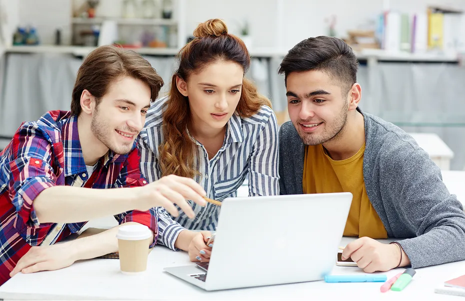 Trois jeunes regardent un ordinateur portable, souriants et engagés dans une discussion.