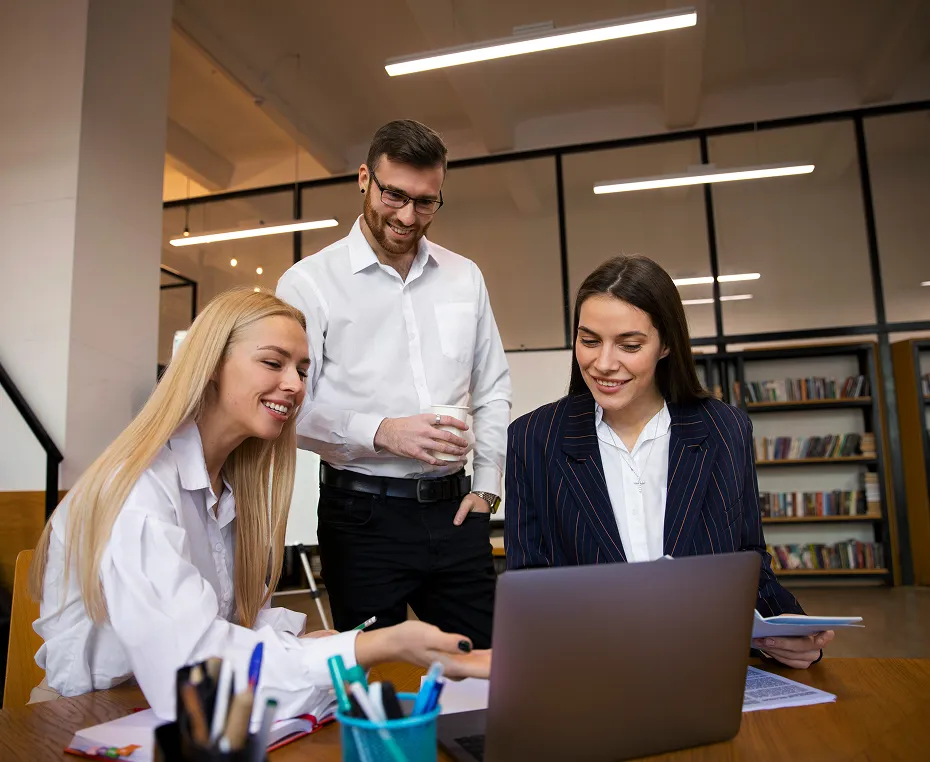 Trois personnes collaborent autour d'un ordinateur portable en milieu de bureau.