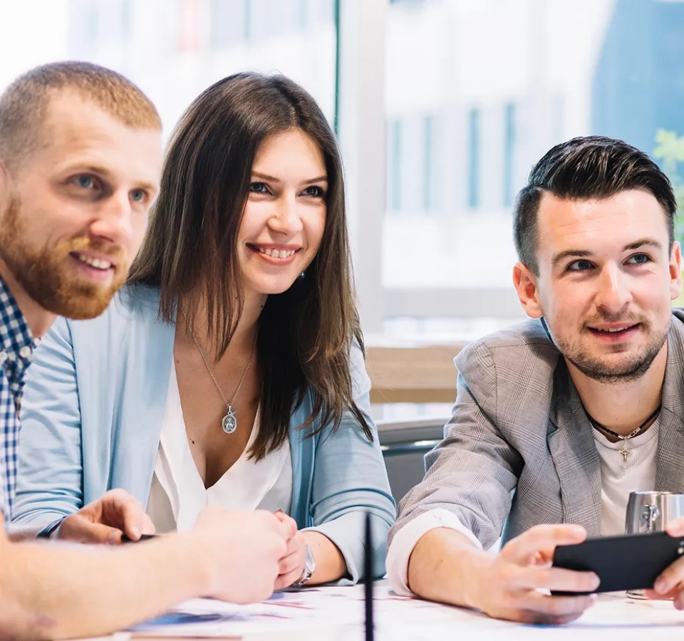 Trois personnes assises à une table, souriant et échangeant des idées en discutant.